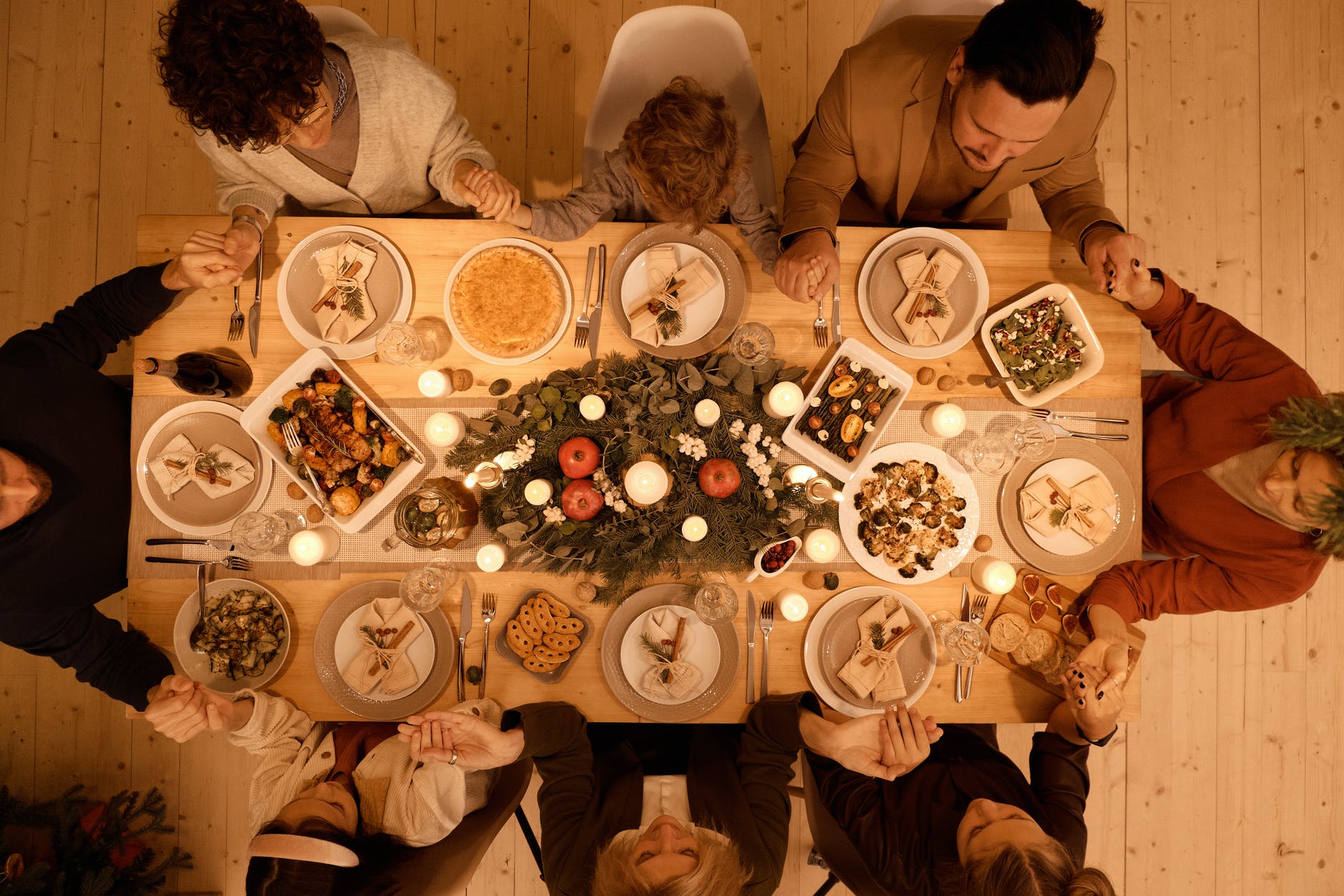 A group of people pray over dinner at a table full of food.